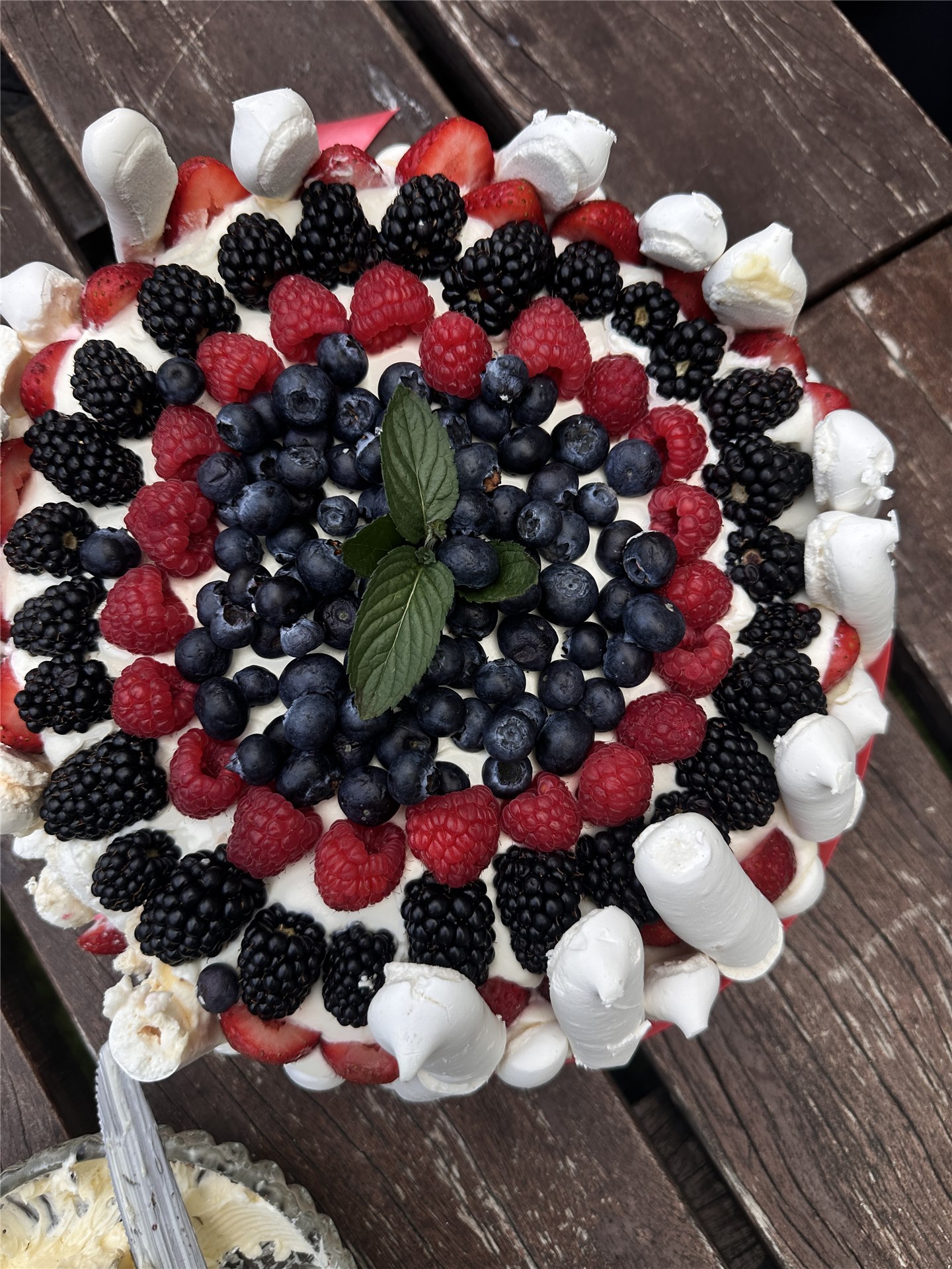 Cake with blackberries, currants, raspberries and whipped cream on the wooden picnic table